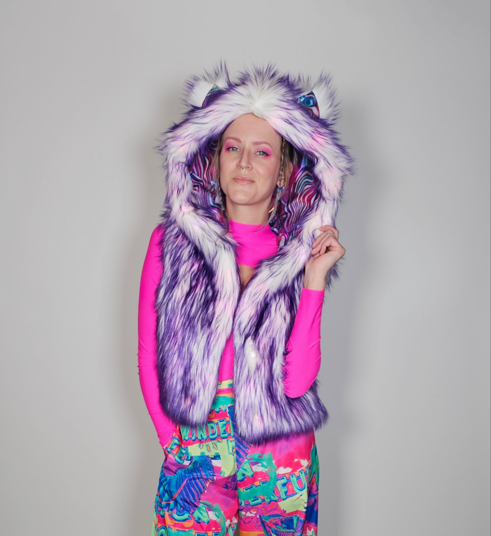 Person wearing a colorful outfit with a fur vest with hood on a plain background