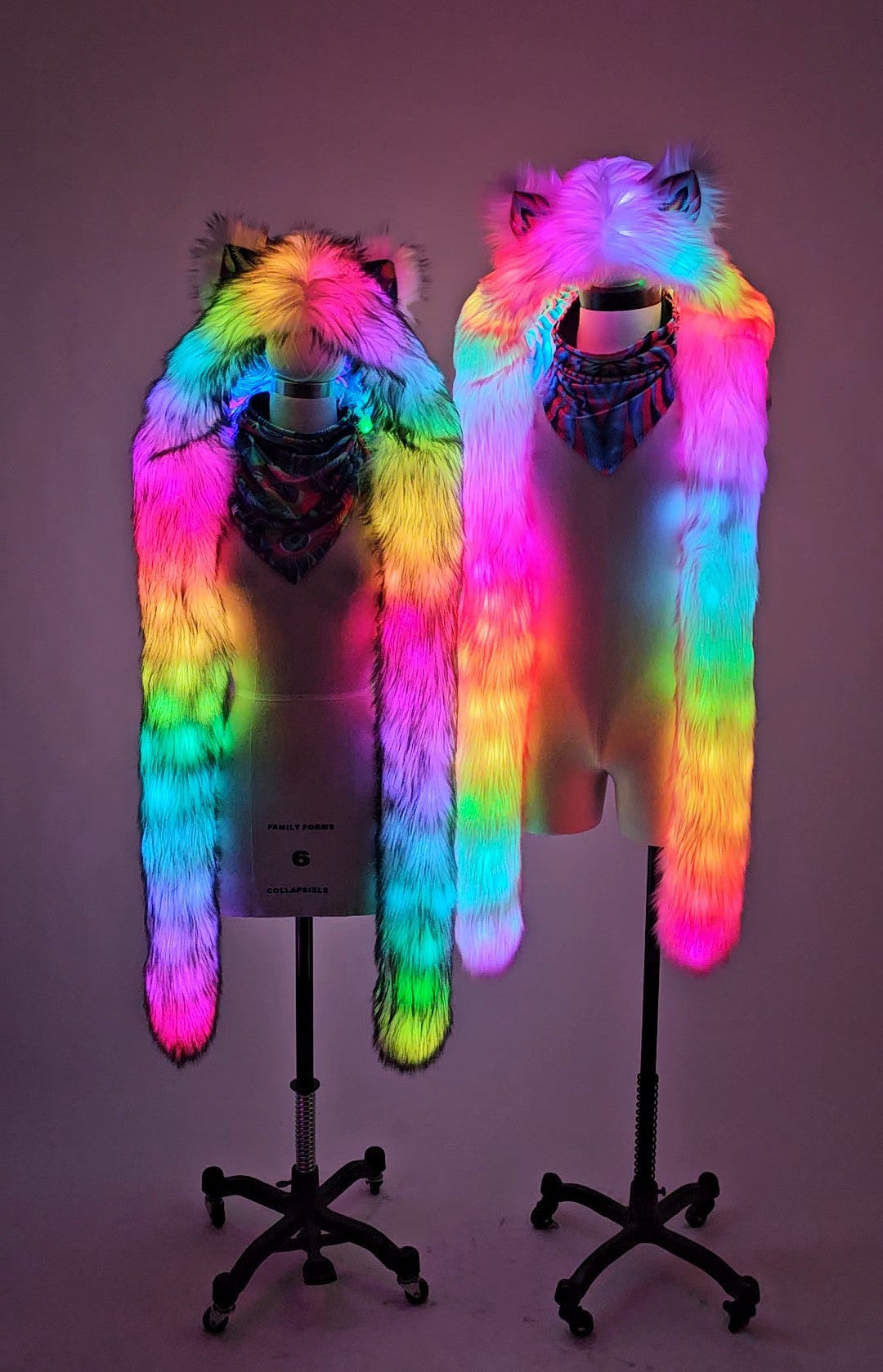 Two mannequins wearing colorful fur hoods with glowing lights on a plain background