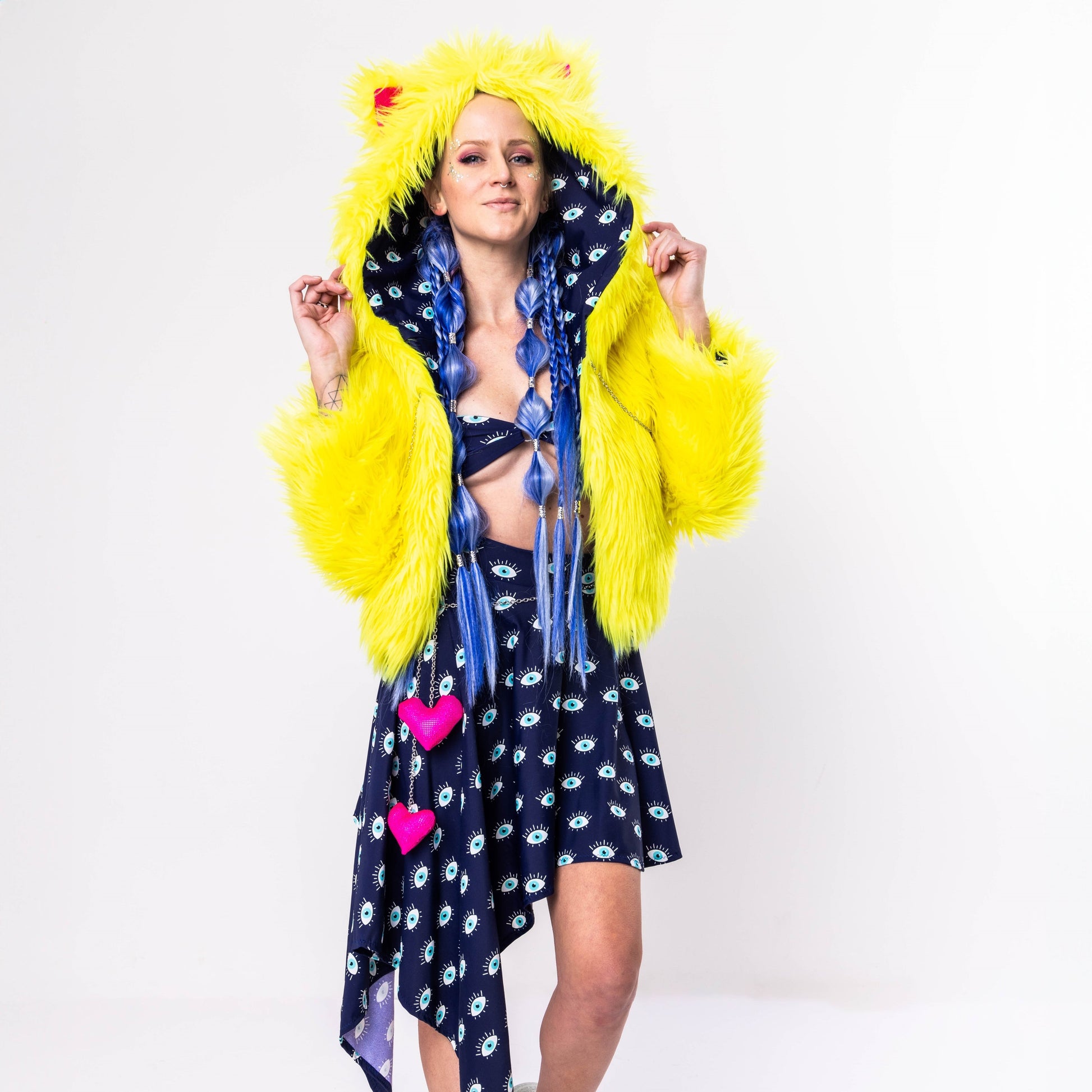 A person wearing a yellow faux fur coat with a hood and animal ears, featuring eye and heart patterns on a darker fabric.