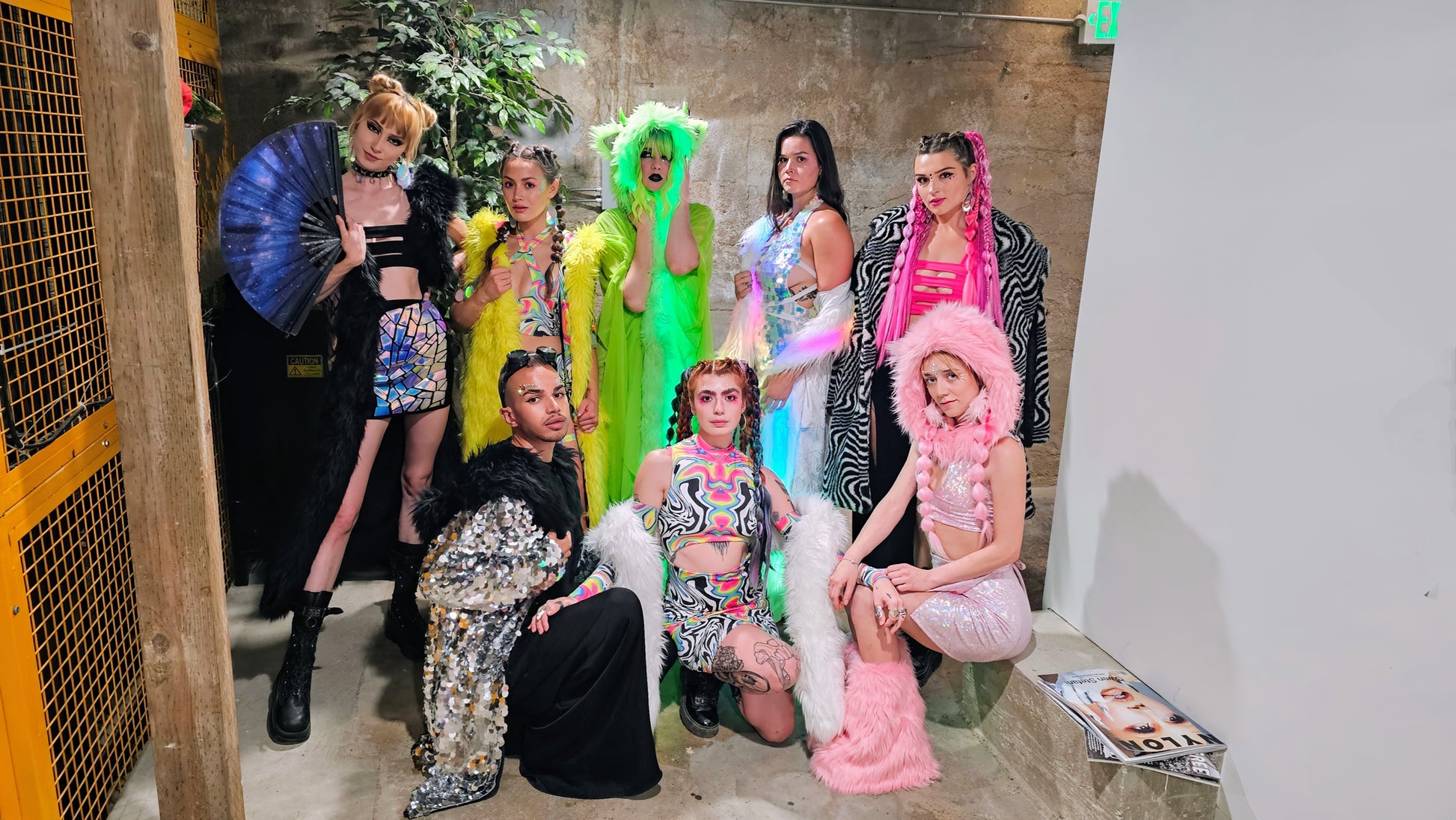 Group of people in colorful costumes posing together in a room with a concrete wall.