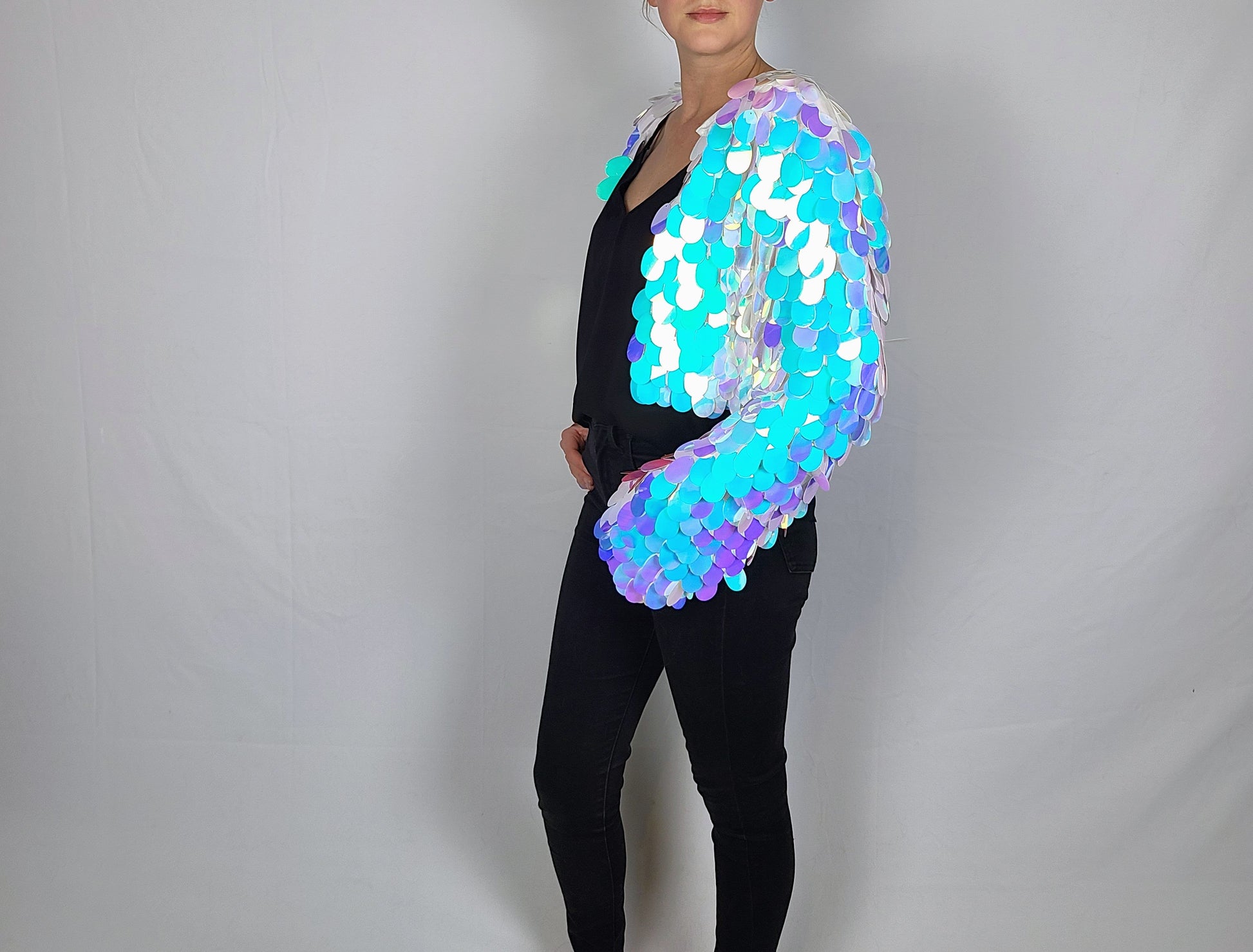 Woman wearing a cropped sequin jacket made with large iridescent blue sequins and white satin lining