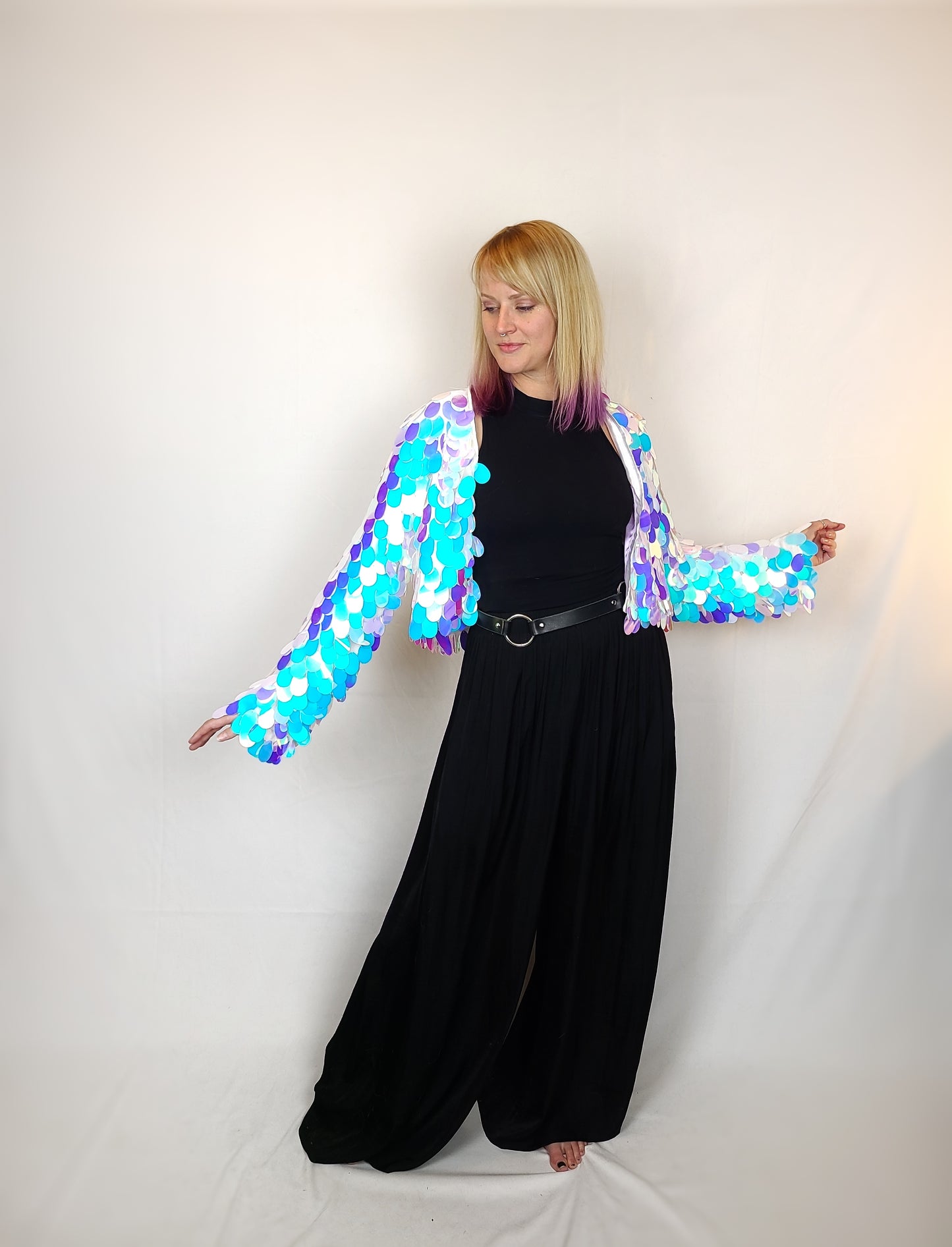 Woman wearing a cropped sequin jacket made with large blue iridescent sequins and white satin lining