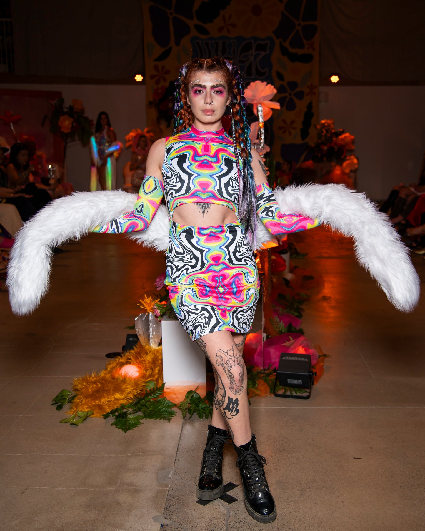 Model wearing a colorful outfit with large white boa on a runway.