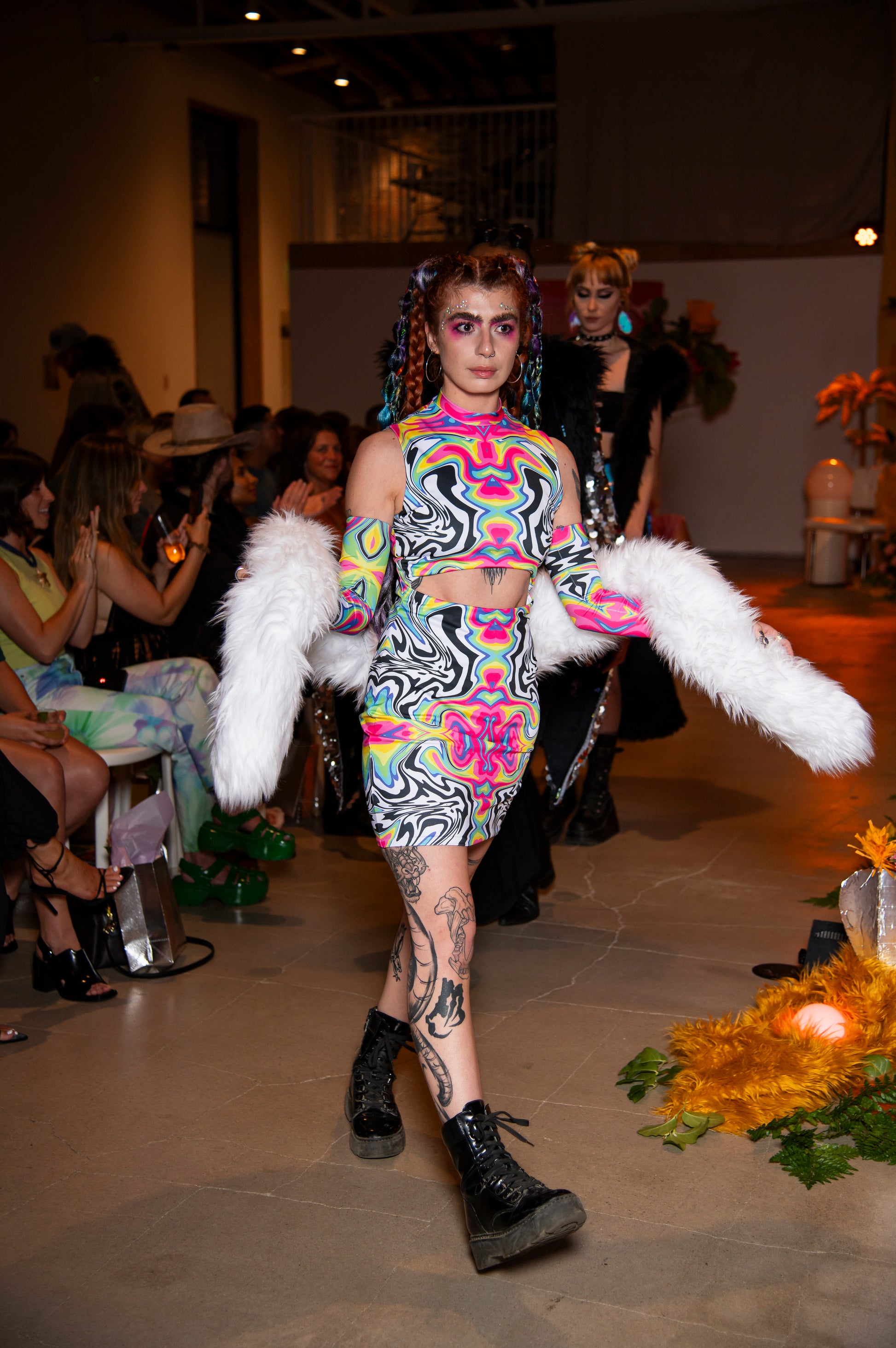 Model walking on a runway wearing a colorful outfit with white faux fur