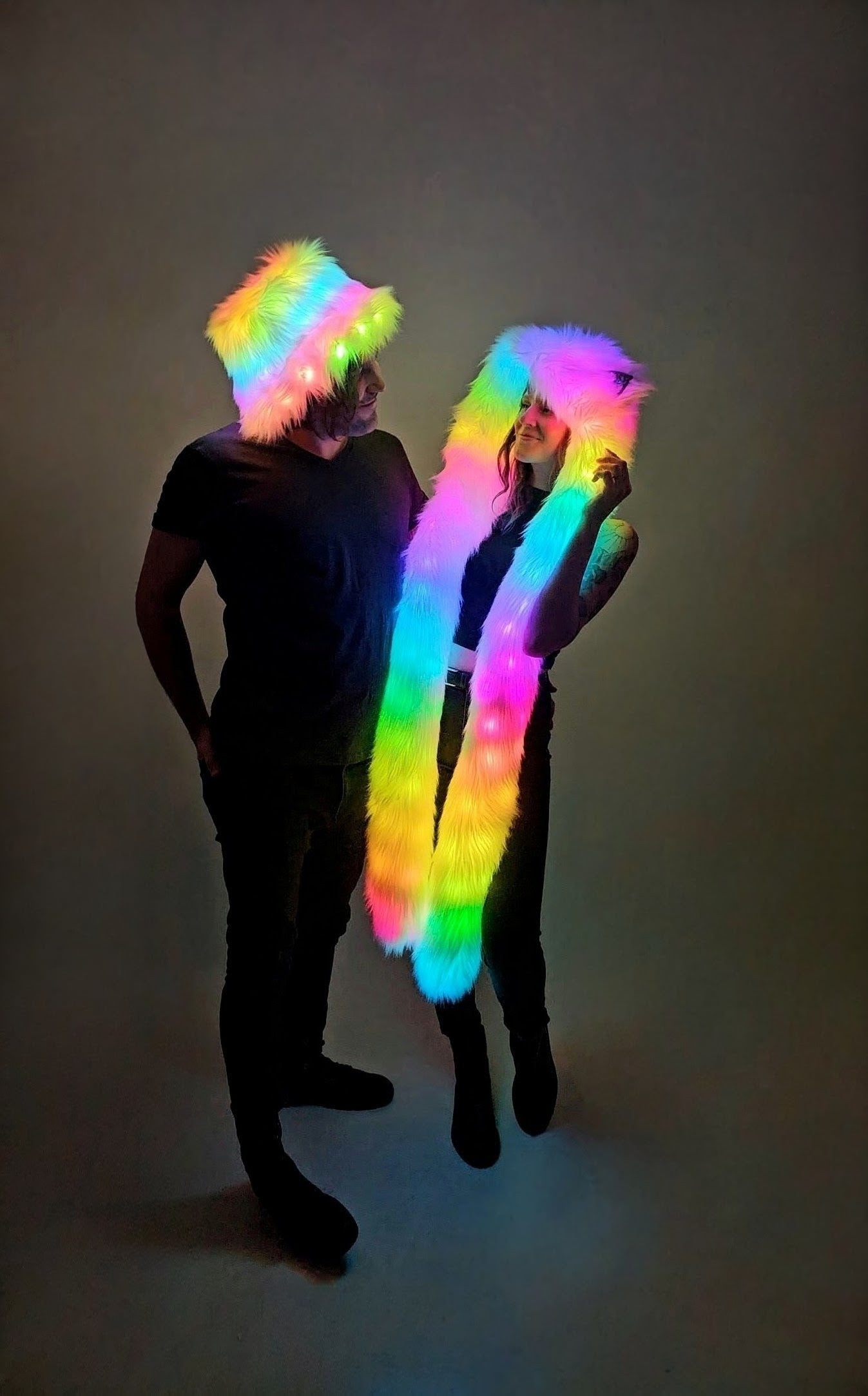 Two people wearing colorful LED accessories against a dark background