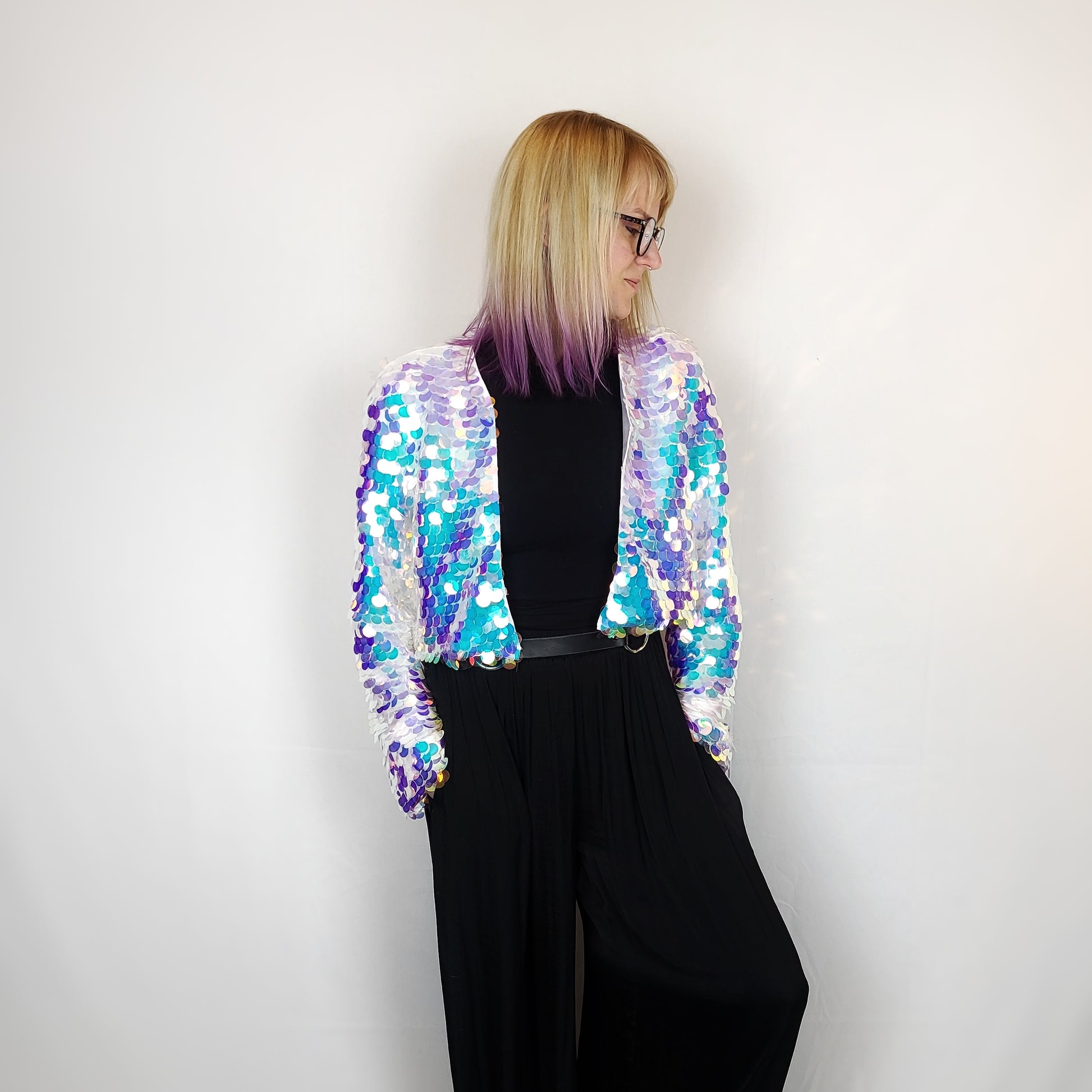 Woman wearing cropped sequin jacket with blue iridescent sequins and white satin lining.