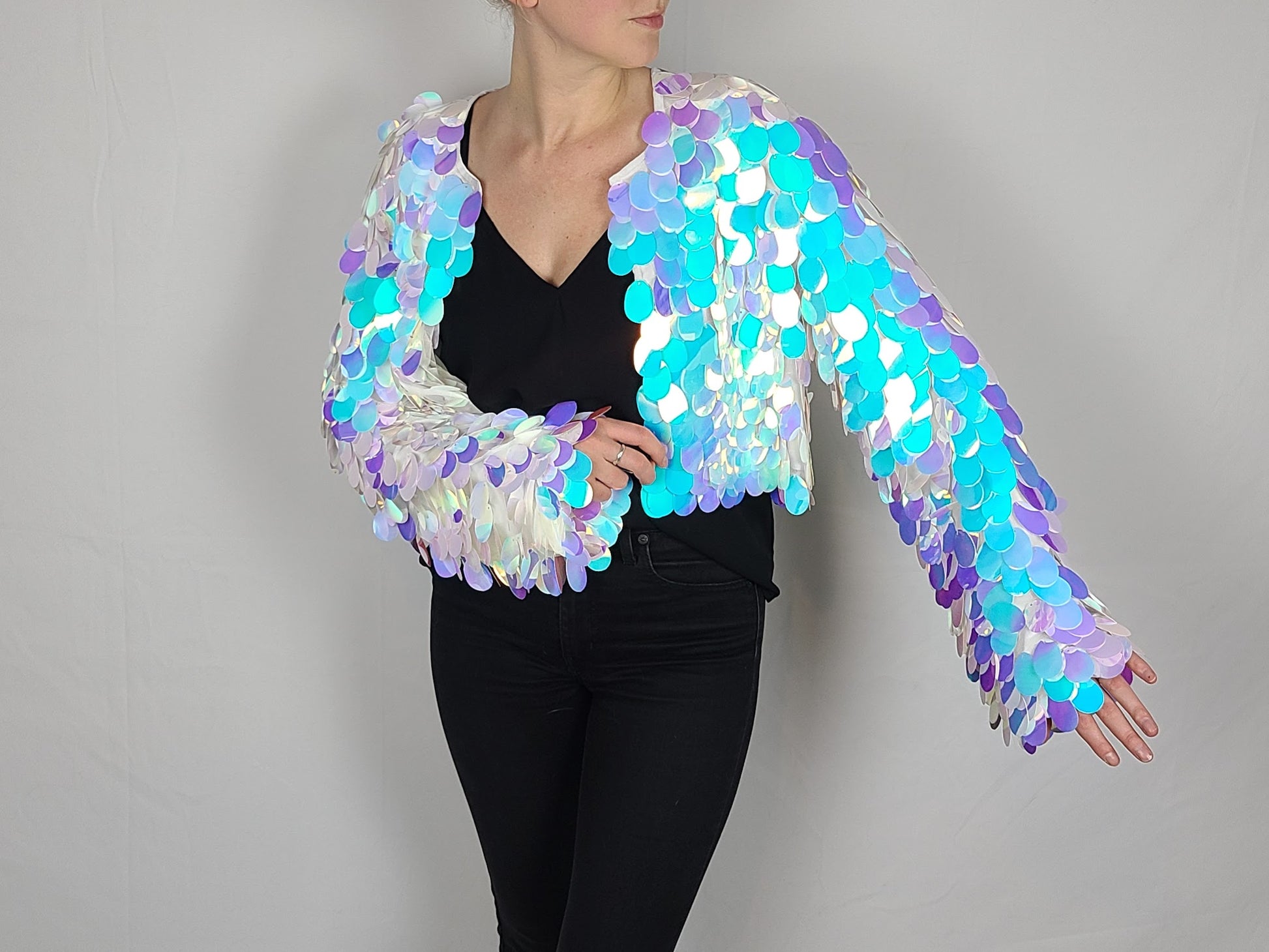 Woman wearing a cropped sequin jacket made with large iridescent blue sequins and white satin lining