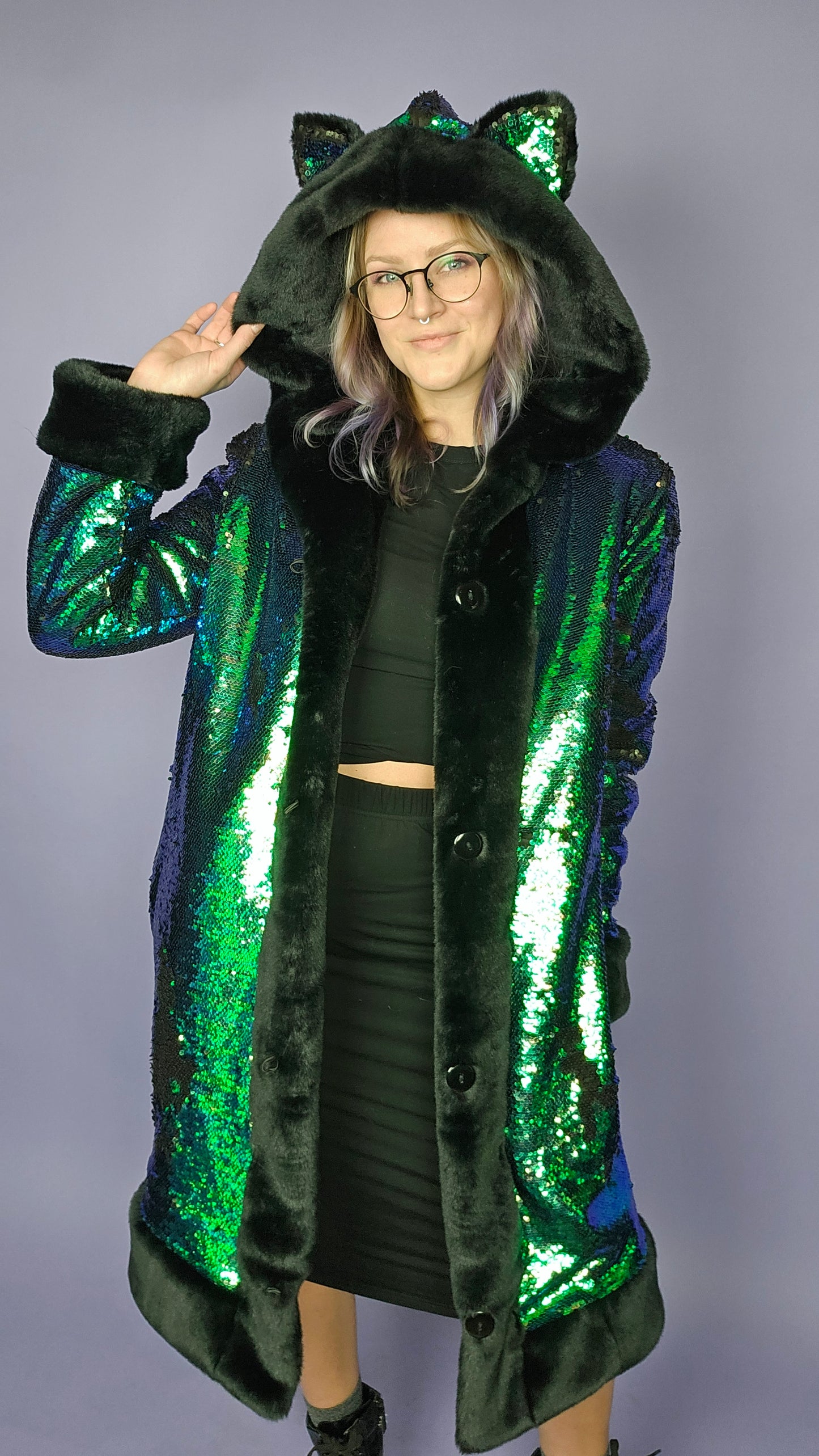 Woman wearing coat made with emerald green sequins, black faux fur trim and lining, and animal ears on the hood.