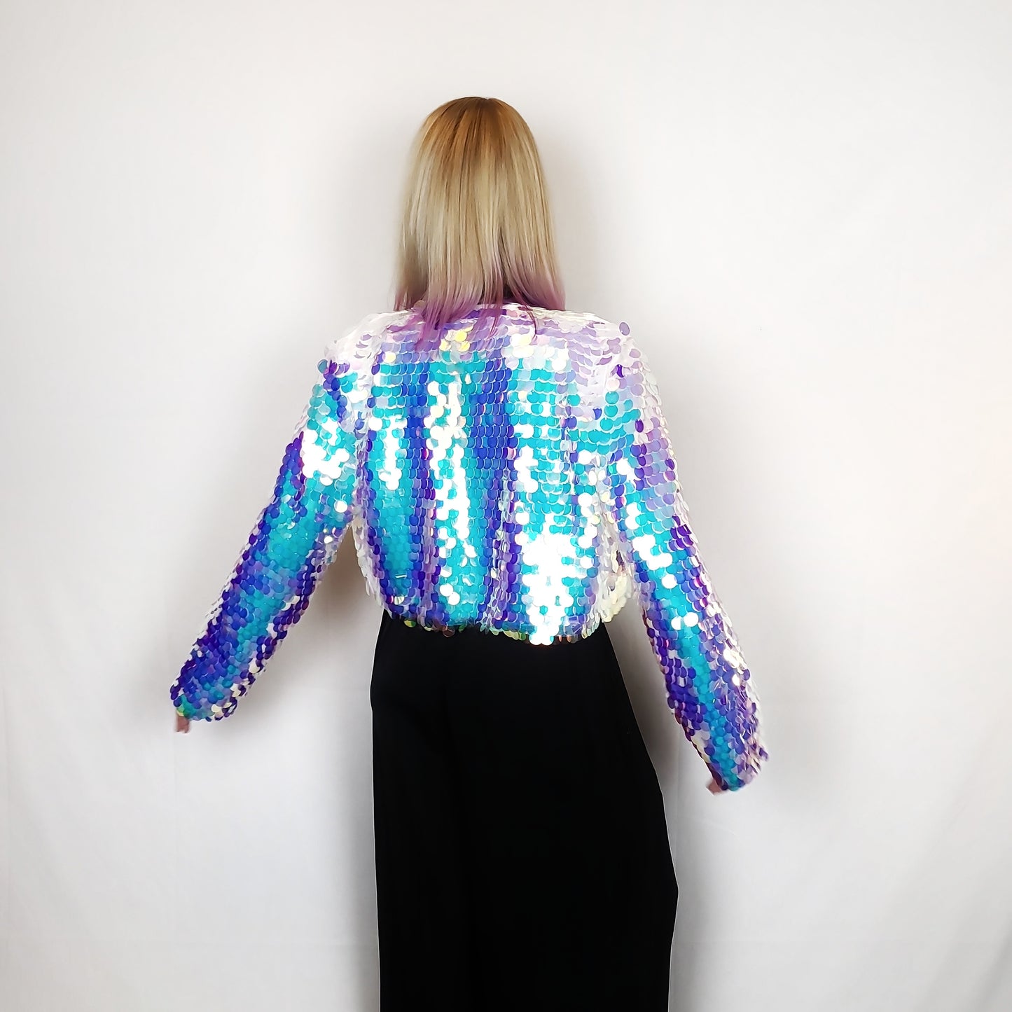 Woman wearing a cropped sequin jacket made with iridescent sequins and white satin lining