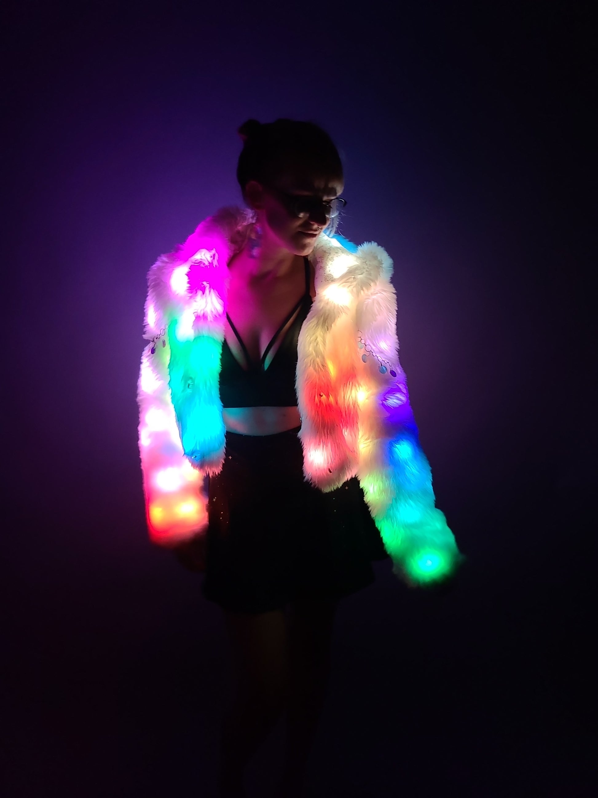 Woman wearing a cropped faux fur coat illuminated by rainbow color leds.