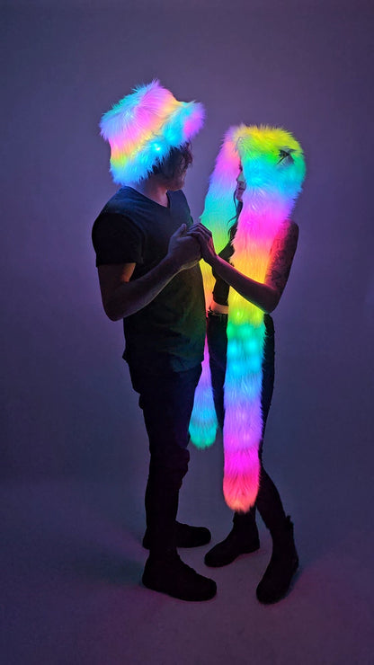 Person wearing a colorful LED hat and another person wearing a colorful led hood against a dark background