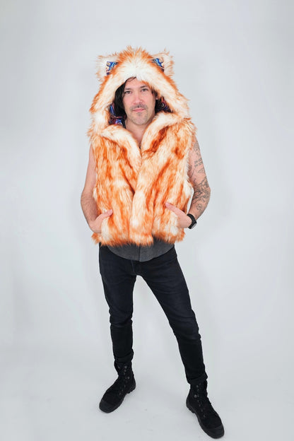 A man modeling a hooded orange and white faux fur vest with animal ears on the hood, paired with black pants and boots, against a light gray studio background.