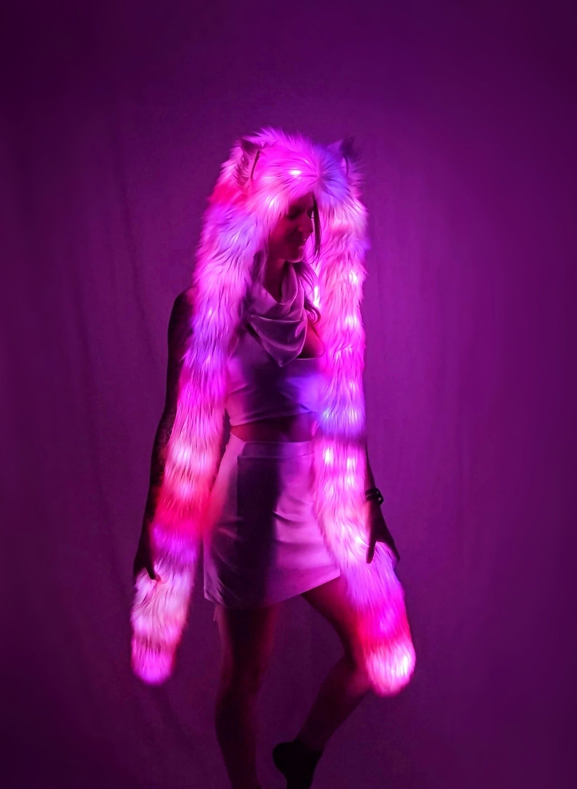 Person wearing a faux fur illuminated hood against a pink background