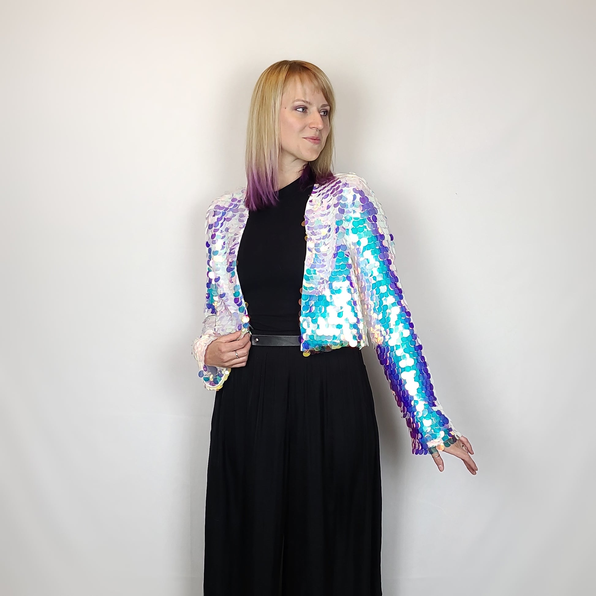 Woman wearing a cropped sequin jacket made with iridescent sequins and white satin lining.