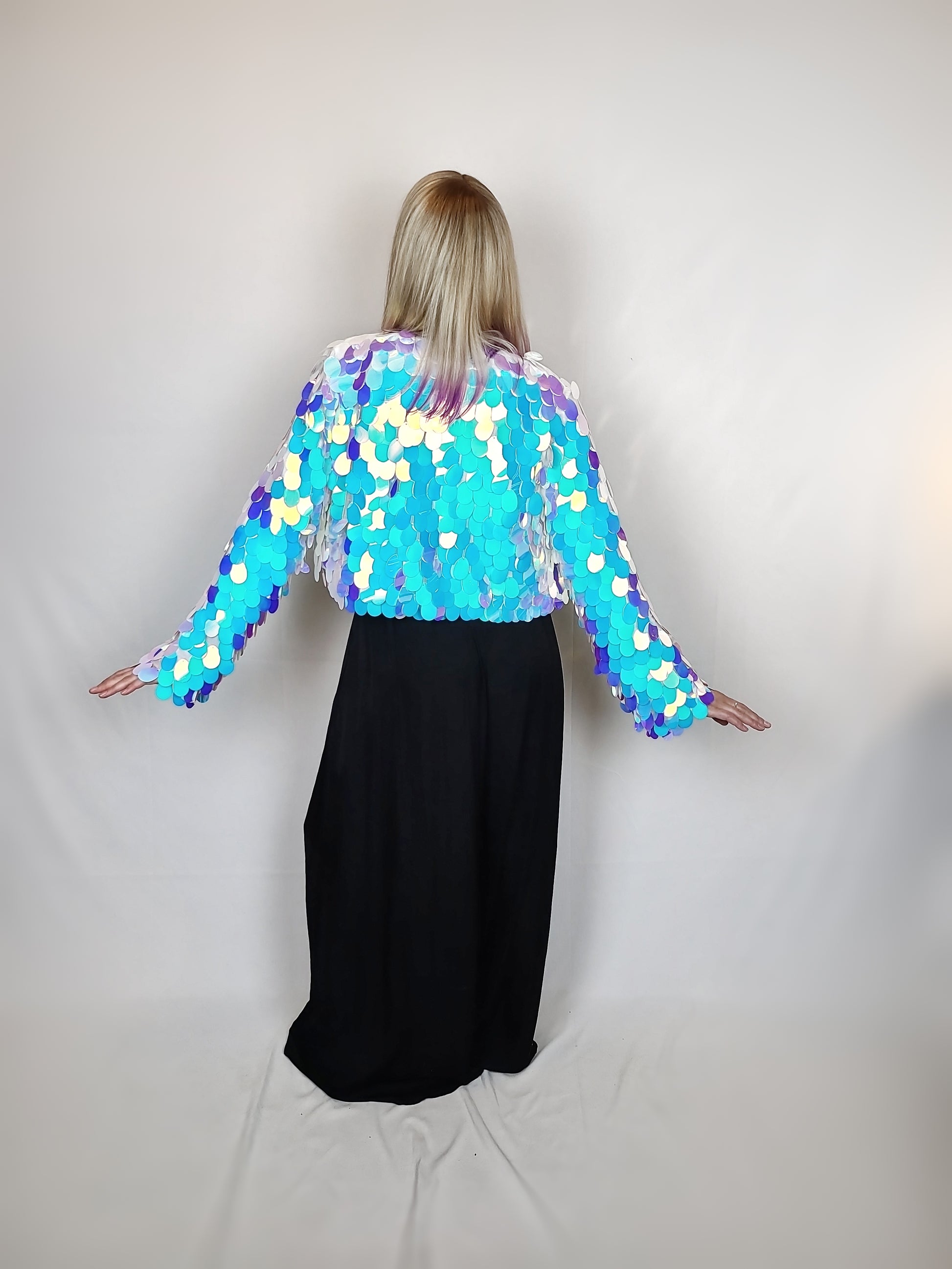 Woman wearing a cropped sequin jacket made with large iridescent blue sequins and white satin lining