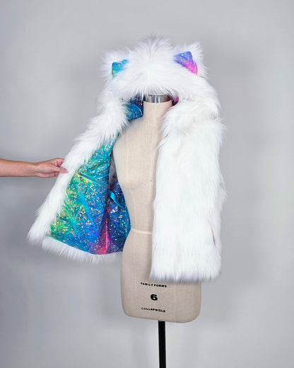 A white faux fur vest with a hood featuring cat ears and a colorful iridescent glitter lining, displayed on a dress form with a hand adjusting the lining.