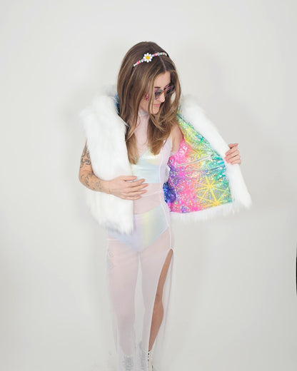 A woman modeling a white faux fur vest with a vibrant, multicolored iridescent sequined lining, worn over a pastel iridescent bodysuit and sheer tights against a plain white studio background.