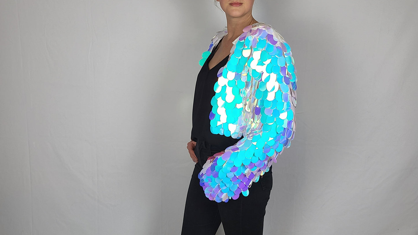 Woman wearing a cropped sequin jacket made with iridescent blue sequins and white satin lining